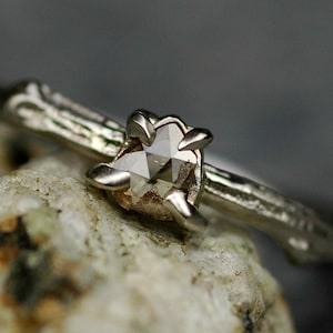 May include: A silver ring featuring a rough, natural diamond set in a delicate, branch-like band.