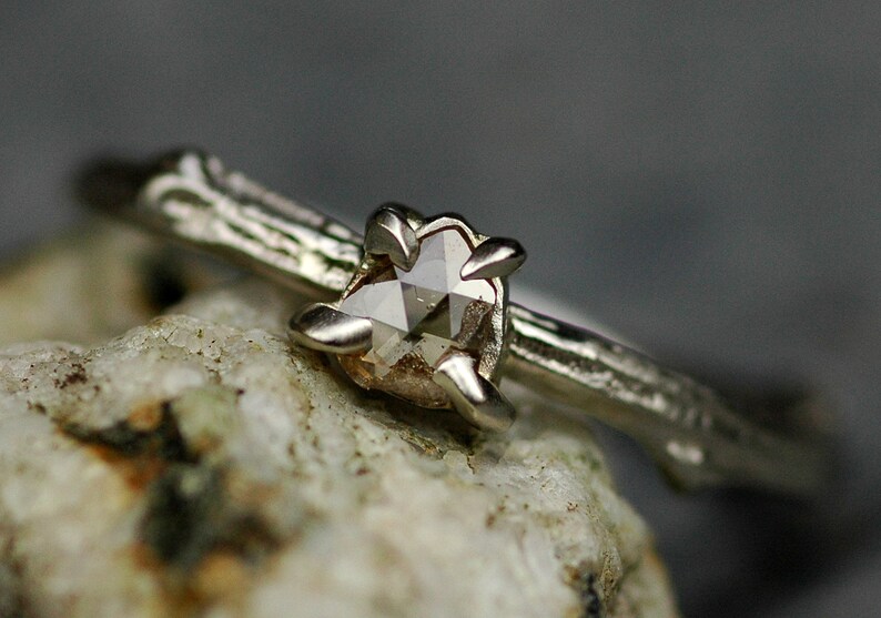 May include: A silver ring featuring a rough, natural diamond set in a delicate, branch-like band.