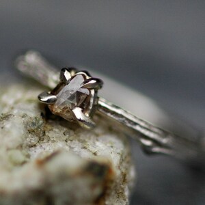 May include: A silver ring featuring a rough, clear diamond set in a branch-like band.