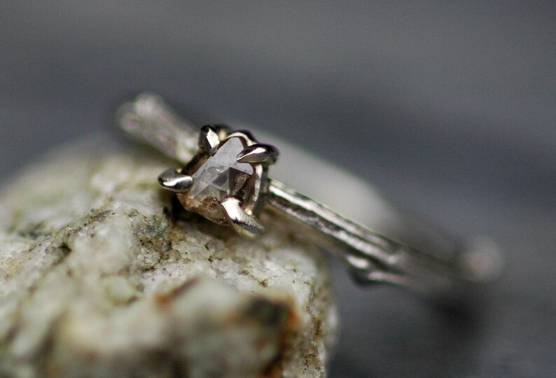 May include: A silver ring featuring a rough, clear diamond set in a branch-like band.