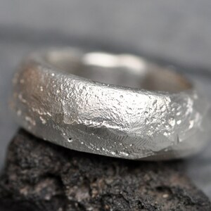 May include: A silver ring with a textured, hammered finish. The ring is wide and has a rounded shape.