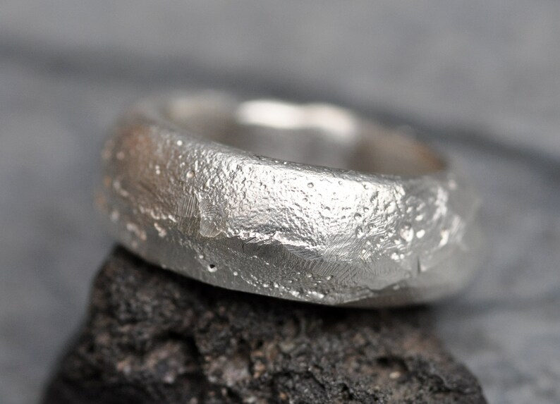 May include: A silver ring with a textured, hammered finish. The ring is wide and has a rounded shape.