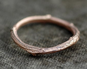 May include: A rose gold twig ring with a textured, organic design. The ring is made to look like a branch of a tree.