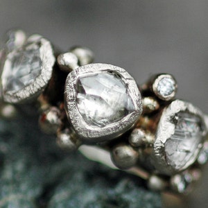 May include: A silver ring with multiple small diamonds set in a textured band. The ring features a large, faceted diamond in the center.