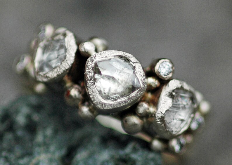 May include: A silver ring with multiple small diamonds set in a textured band. The ring features a large, faceted diamond in the center.