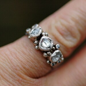 May include: A silver ring with multiple small diamonds set in a cluster design. The diamonds are clear and have a faceted cut.