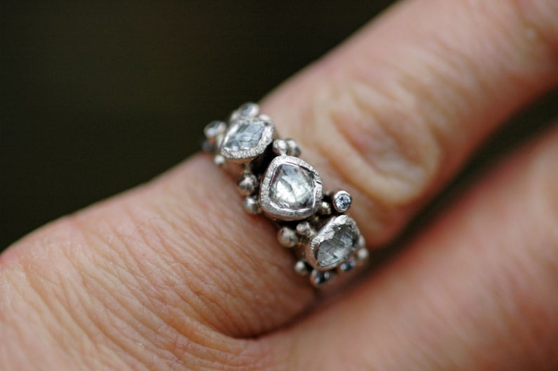 May include: A silver ring with multiple small diamonds set in a cluster design. The diamonds are clear and have a faceted cut.