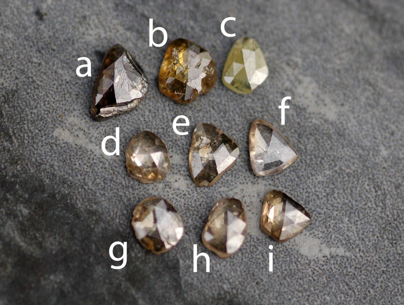 May include: Nine rough cut diamonds in various shapes and sizes. The diamonds are brown, grey, and yellow in colour.