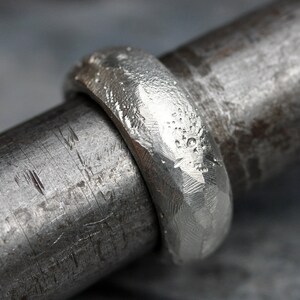 May include: A silver ring with a hammered texture. The ring is on a metal rod.