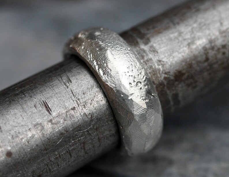 May include: A silver ring with a hammered texture. The ring is on a metal rod.