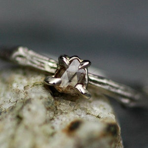 May include: A silver ring featuring a delicate twig design and a rough, light brown diamond.
