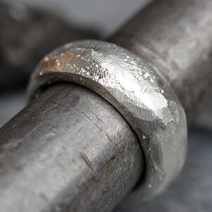 May include: A close-up of a silver ring with a hammered texture. The ring is thick and has a rounded profile.