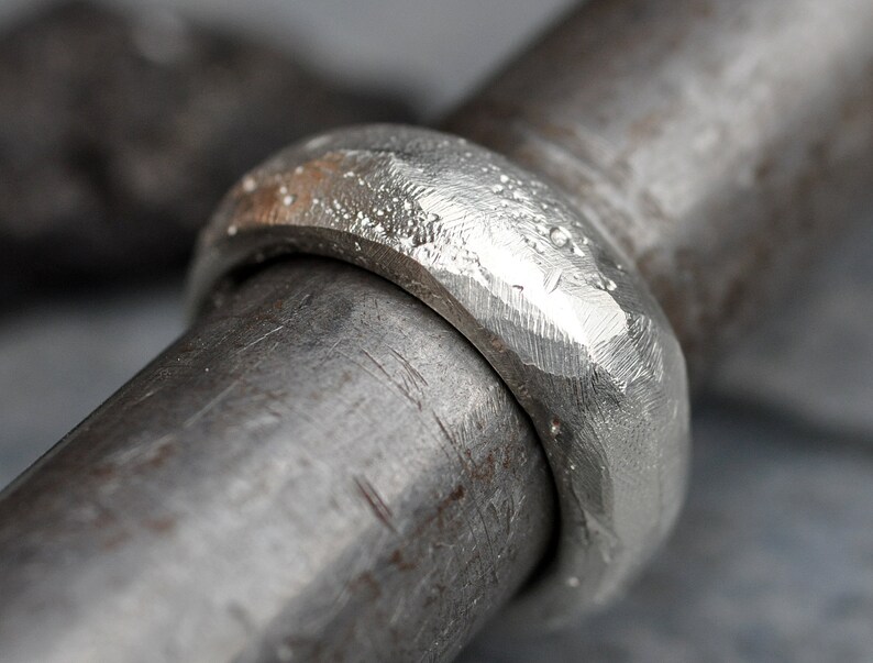 May include: A close-up of a silver ring with a hammered texture. The ring is thick and has a rounded profile.