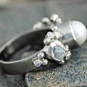 May include: A silver ring with a pearl, a rough diamond, and small diamonds set in a textured band.
