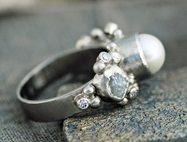 May include: A silver ring with a pearl, a rough diamond, and small diamonds set in a textured band.