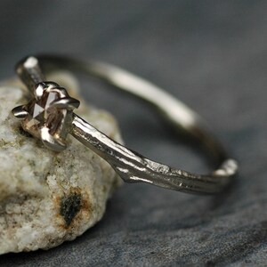 May include: A silver ring with a rough, textured band and a single, clear, faceted gemstone.