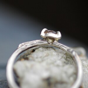 May include: A silver ring with a textured band and a small, clear gemstone set in a prong setting.