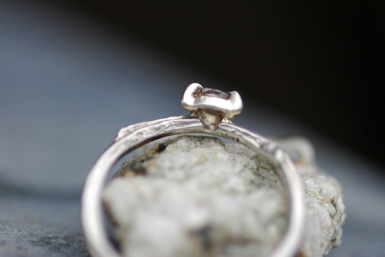 May include: A silver ring with a textured band and a small, clear gemstone set in a prong setting.