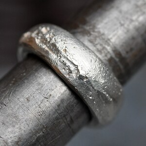 May include: A silver ring with a textured, hammered finish. The ring is thick and has a wide band.