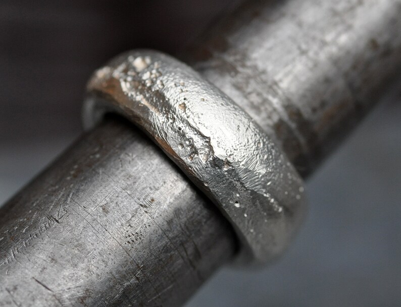 May include: A silver ring with a textured, hammered finish. The ring is thick and has a wide band.