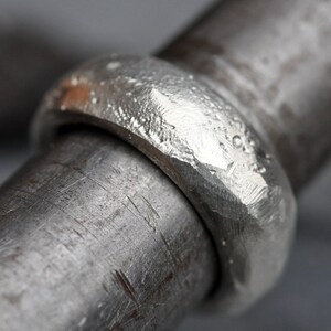 May include: A close-up of a silver ring with a hammered texture. The ring is thick and has a rounded shape.