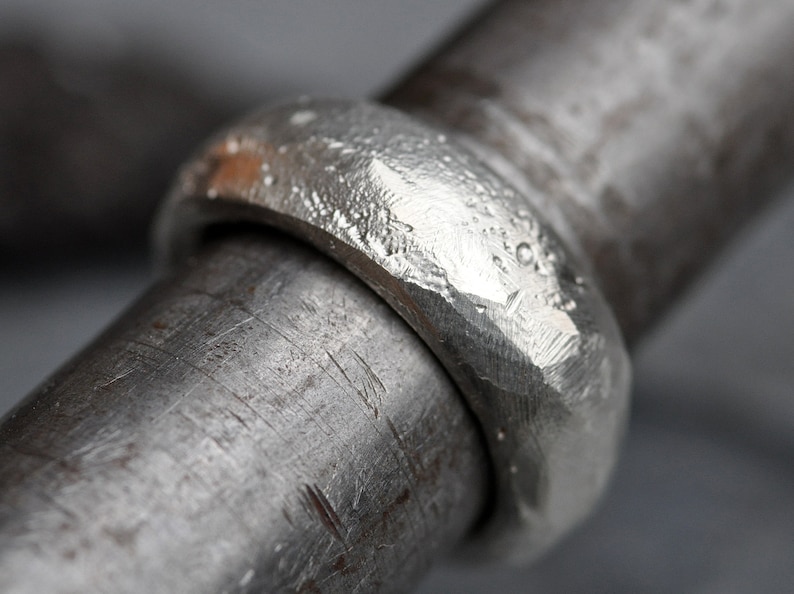 May include: A close-up of a silver ring with a hammered texture. The ring is thick and has a rounded shape.