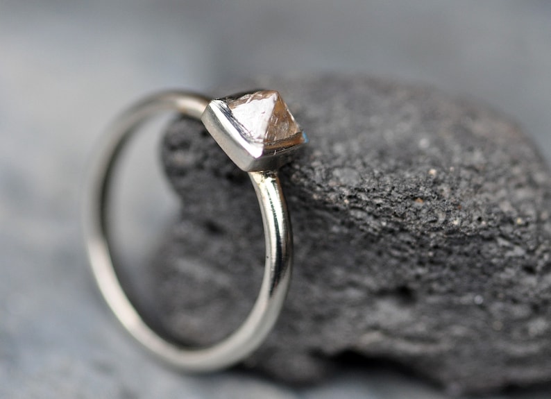 May include: A silver ring with a clear, faceted, pyramid-shaped gemstone.
