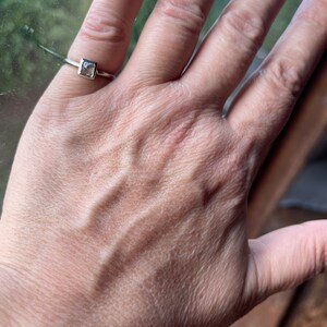 May include: A silver ring with a square-shaped clear gemstone.