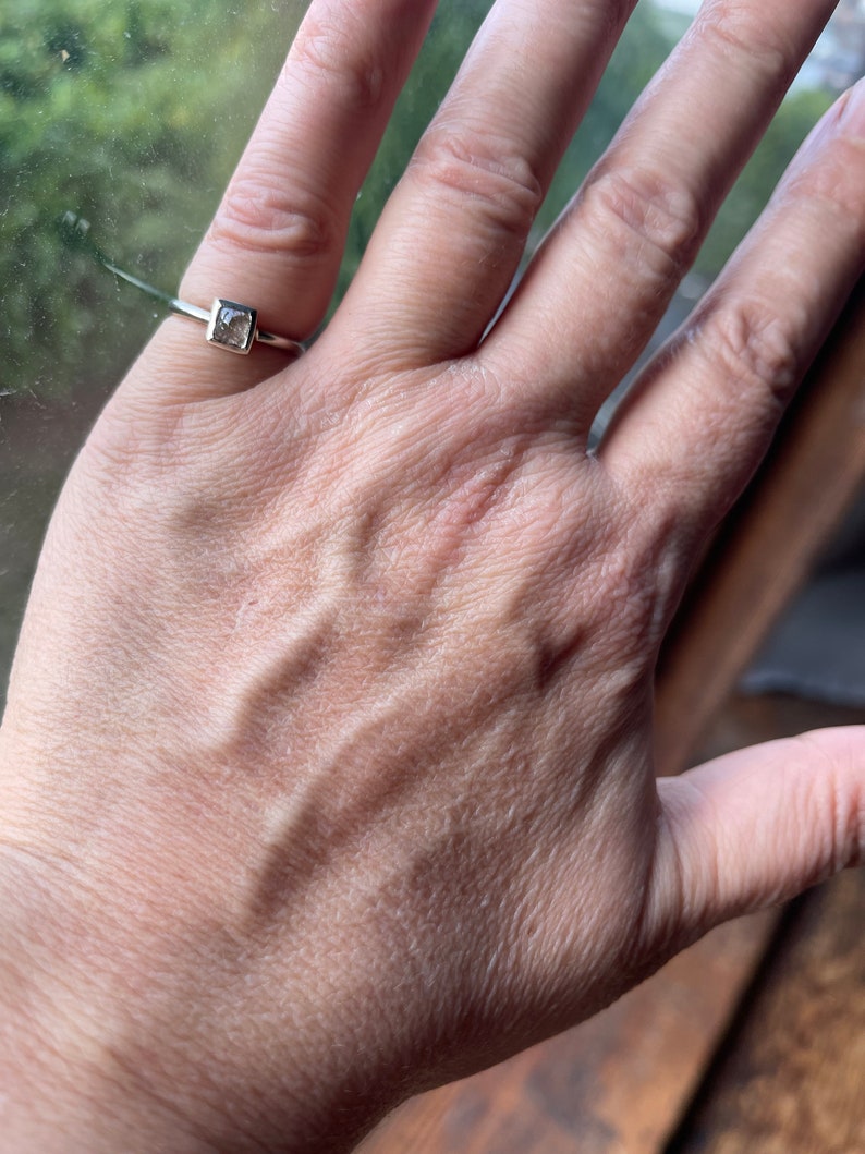 May include: A silver ring with a square-shaped clear gemstone.
