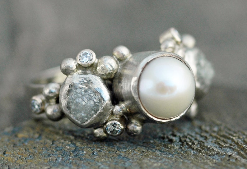 May include: A silver ring with a large white pearl, a rough-cut diamond, and smaller diamonds set in a cluster.