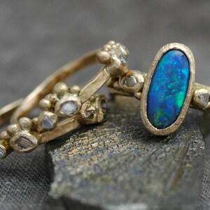 K&ouml;nnte beinhalten: Drei goldene Ringe mit einem blauen Opal-Edelstein, der in den mittleren Ring gefasst ist. Die Ringe sind mit kleinen Diamanten verziert und haben eine strukturierte Oberfl&auml;che.