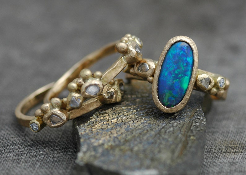 K&ouml;nnte beinhalten: Drei goldene Ringe mit einem blauen Opal-Edelstein, der in den mittleren Ring gefasst ist. Die Ringe sind mit kleinen Diamanten verziert und haben eine strukturierte Oberfl&auml;che.