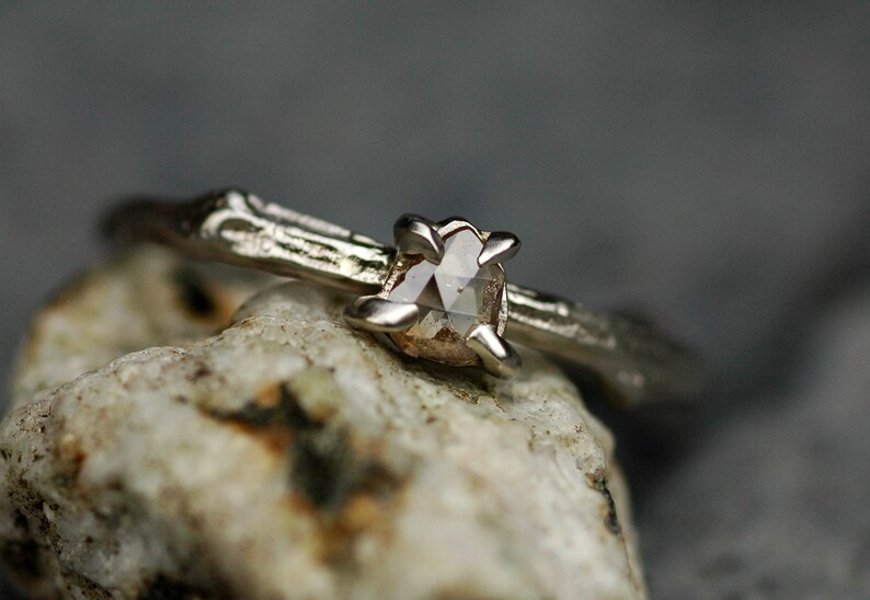 May include: A silver ring with a rough, natural-looking band and a clear, faceted gemstone set in the centre.