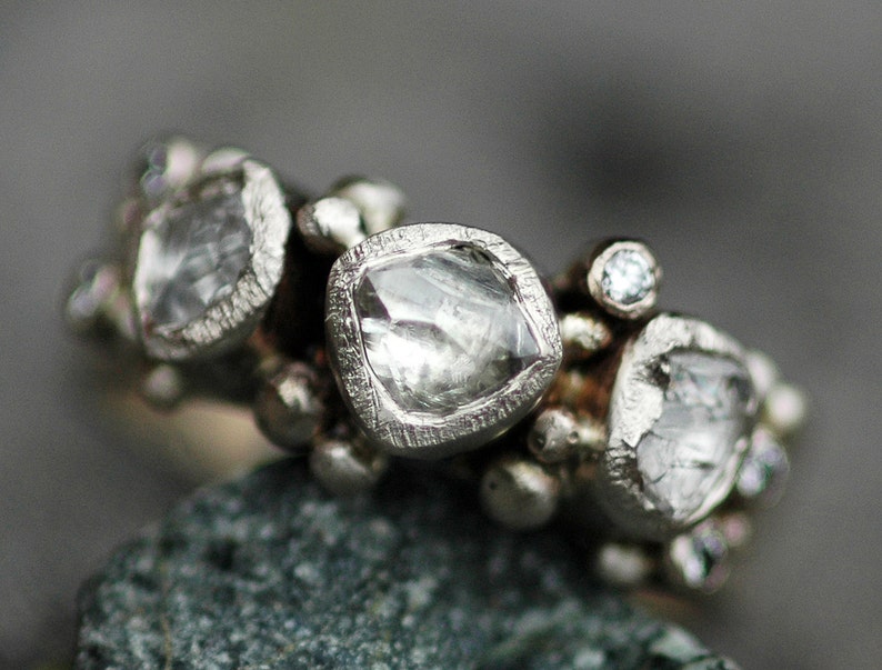 May include: A silver ring with multiple clear, faceted gemstones set in a cluster. The ring is made of metal and has a textured finish.