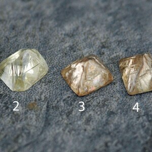 May include: Five different cut diamonds, numbered 1 through 5, are displayed on a gray textured surface. The diamonds are various shades of brown and yellow.