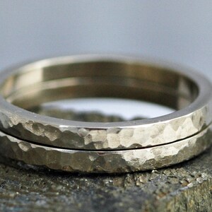 May include: Two silver hammered wedding bands stacked on top of each other. The bands are smooth on the inside and have a hammered texture on the outside.