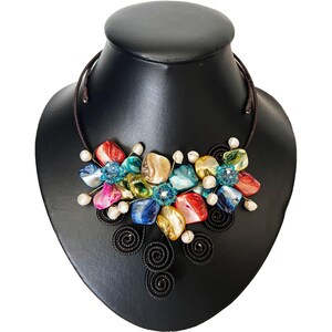 May include: A colorful statement necklace featuring a cluster of iridescent, polished stones in shades of red, blue, yellow, and green. The stones are accented with small white pearls and blue beads, strung on a brown cord.