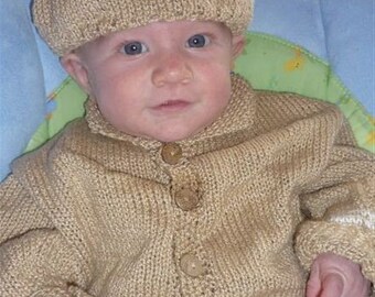 May include: A baby wearing a knitted tan cardigan and a tan knitted hat. The cardigan has buttons down the front.