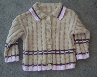 May include: A beige knitted cardigan with a pink and brown trim. The cardigan has a button-up front and long sleeves.