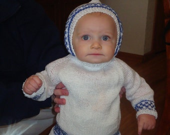 May include: A white knitted baby sweater with blue and white trim. The sweater has a round neckline and long sleeves. The baby is wearing a blue and white knitted hat.