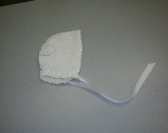 May include: White crocheted baby bonnet with a white satin ribbon.