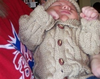 May include: A sleeping baby wearing a beige knit hat and matching button-up sweater. The sweater has a cable knit design and wooden buttons. The baby is also wearing blue jeans. The date 11/26/2008 is visible in the bottom right corner.