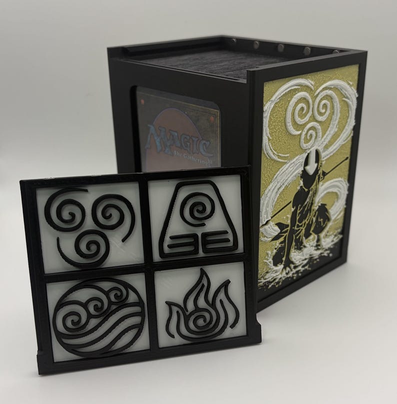 May include: Black and gold card storage box with a removable front panel featuring elemental symbols. The side panel displays a silhouette of a figure with a staff. The box contains a Magic: The Gathering card.