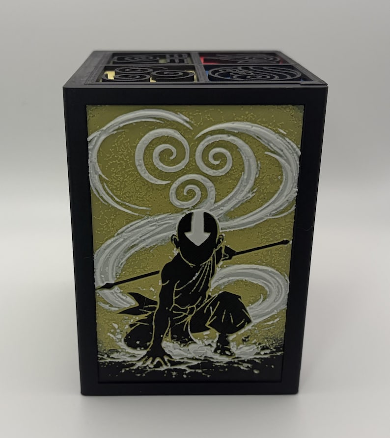 May include: Black rectangular box featuring a silhouette of a character in a kneeling pose with a staff, set against a yellow-green background with white swirling designs. The box has a decorative top with circular patterns.