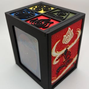 Peut inclure: Une boîte de rangement pour cartes rectangulaire noire avec un panneau latéral présentant un relief texturé rouge d'une silhouette en mouvement et un symbole de flamme. Le couvercle affiche quatre sections carrées avec des icônes élémentaires noires.