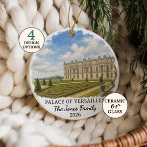 May include: A round white ornament featuring a printed illustration of the Palace of Versailles with manicured gardens under a blue sky. The text reads PALACE OF VERSAILLES, The Jones Family, and 2026. It includes a gold hanging string.