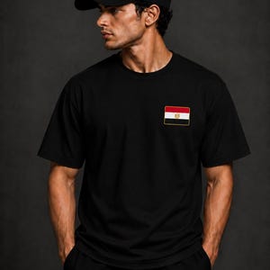 May include: A black short-sleeved t-shirt and a matching black baseball cap. Both items feature a rectangular patch displaying the national flag of Egypt, which consists of horizontal red, white, and black stripes with a gold eagle emblem in the center.