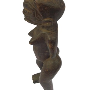 以下が含まれることがあります： 暗褐色の木製彫刻で、人間の姿をしています。丸い頭、明確な顔、目立つ胸があります。腕はありません。脚を曲げ、足を地面に平らにして立っています。