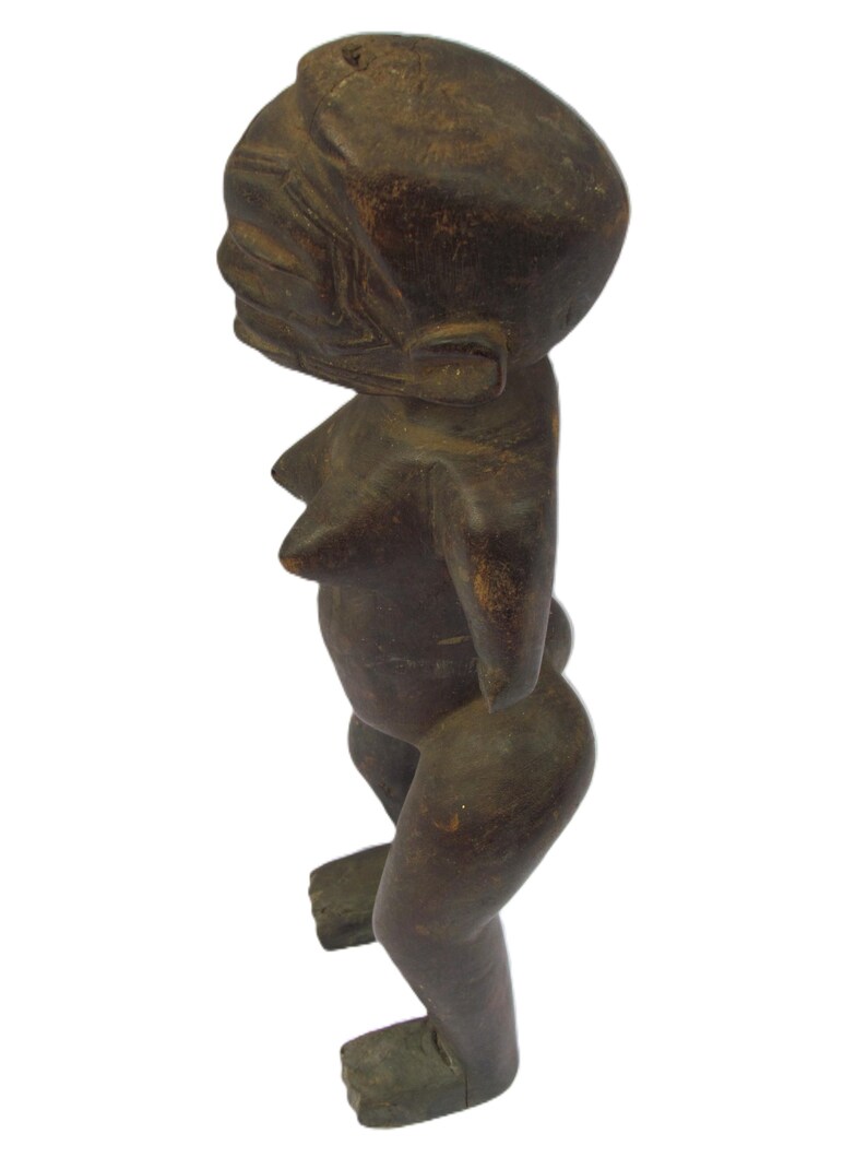 以下が含まれることがあります： 暗褐色の木製彫刻で、人間の姿をしています。丸い頭、明確な顔、目立つ胸があります。腕はありません。脚を曲げ、足を地面に平らにして立っています。