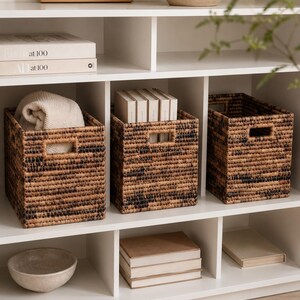 May include: Three rectangular woven storage baskets with a variegated brown and black pattern. Each basket features integrated rectangular handles on the sides and a structured, boxy shape, designed for organizing items on a shelf.